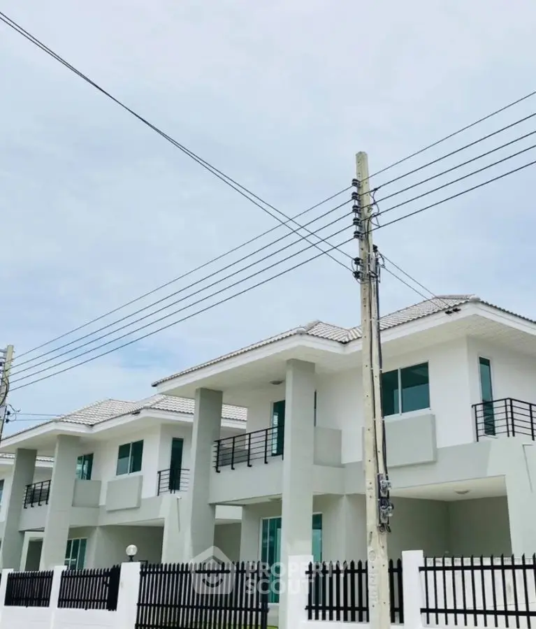 Modern two-story white houses with balconies and black railings under a clear sky.