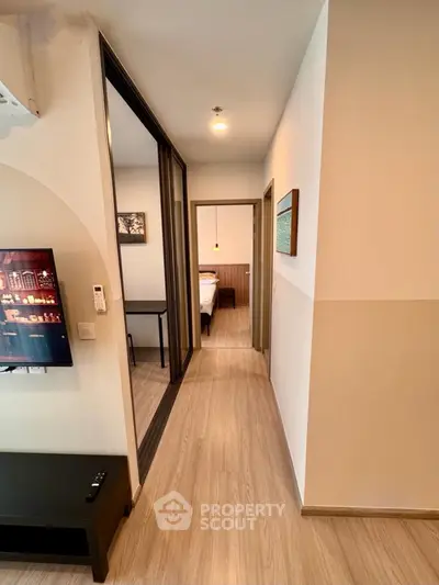 Modern apartment hallway leading to a cozy bedroom with stylish decor and wooden flooring.