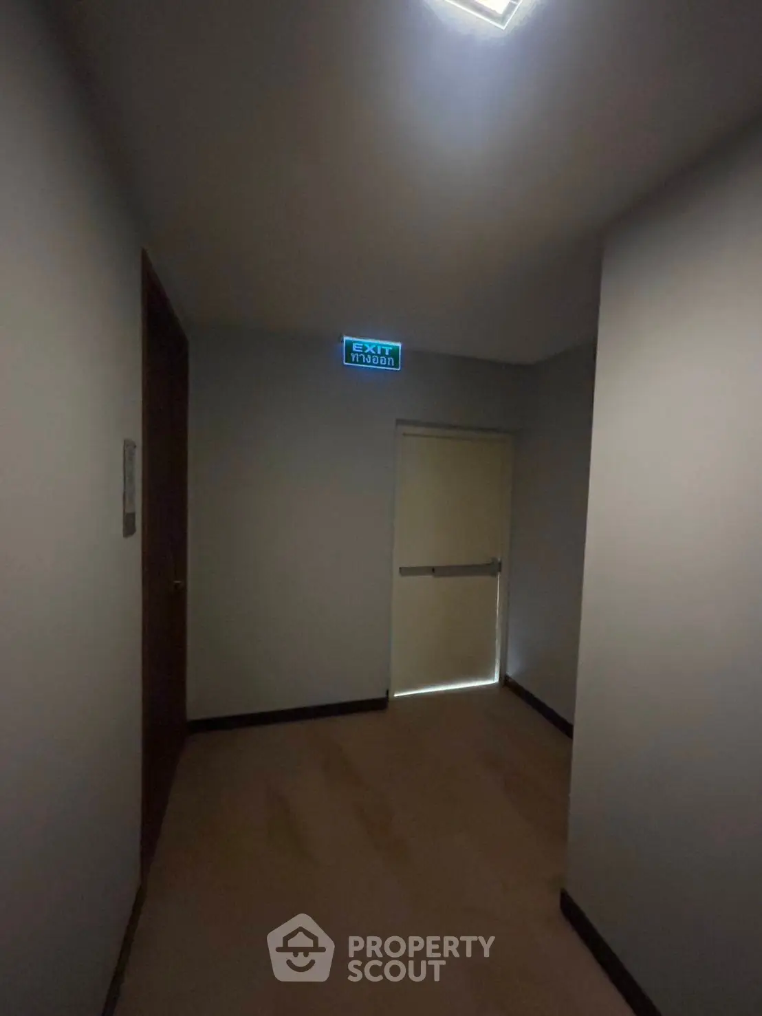 Dimly lit corridor with emergency exit sign and door, ideal for safety-conscious property buyers.