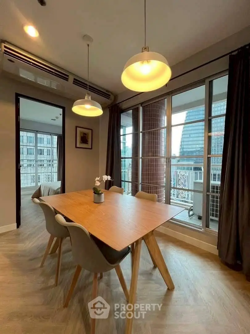 Modern dining area with wooden table, stylish lighting, and city view from large windows.
