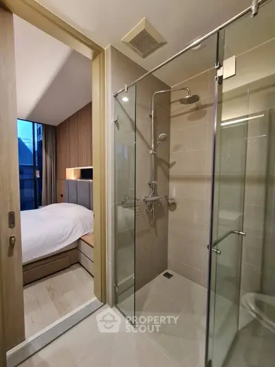 Modern apartment with sleek bathroom and cozy bedroom, featuring glass shower and wooden accents.