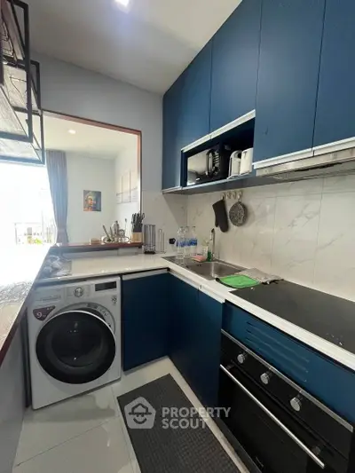 Modern kitchen with blue cabinets, washing machine, and sleek appliances in a compact layout.