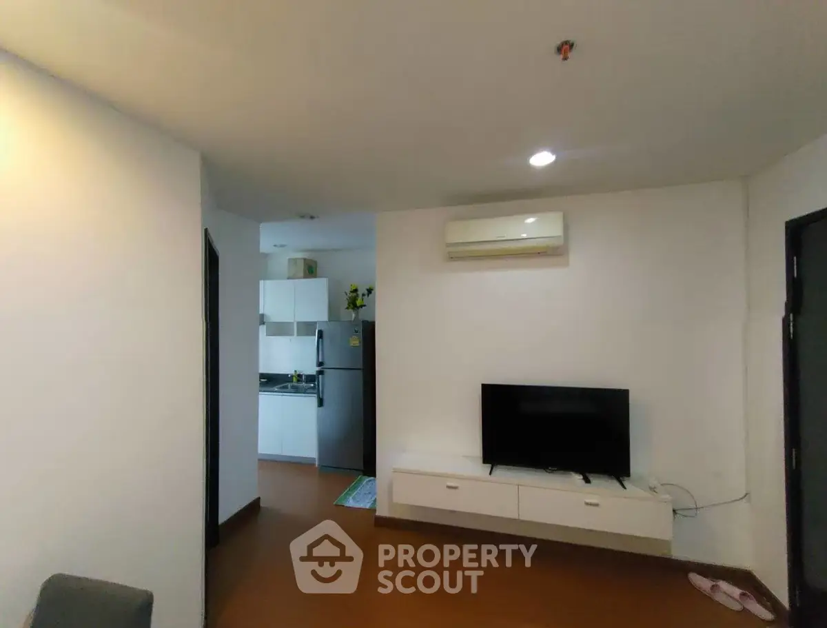 Modern living room with wall-mounted TV and view into compact kitchen