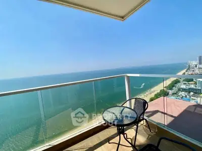 Stunning ocean view from a high-rise balcony with glass railing and outdoor seating.