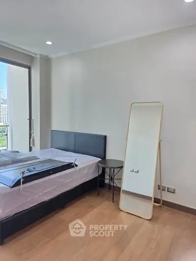 Modern bedroom with large window and stylish mirror, offering a bright and inviting atmosphere.