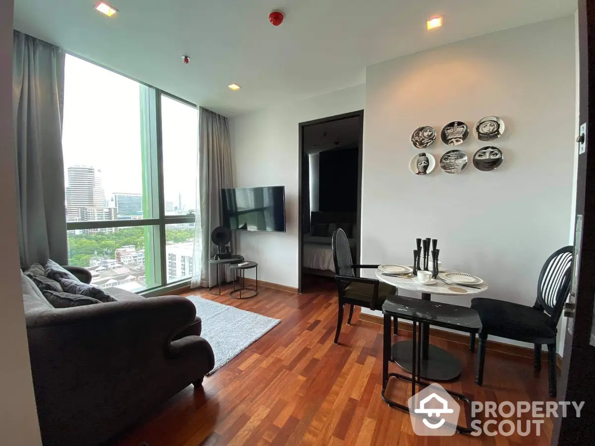 Spacious living room with polished hardwood floors, modern furniture, and abundant natural light from floor-to-ceiling windows leading to a balcony with a view.