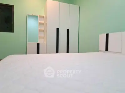 Spacious bedroom with modern white wardrobe and mint green walls.