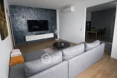 Modern living room with stylish decor and large TV, featuring a cozy gray sofa and elegant wooden flooring.