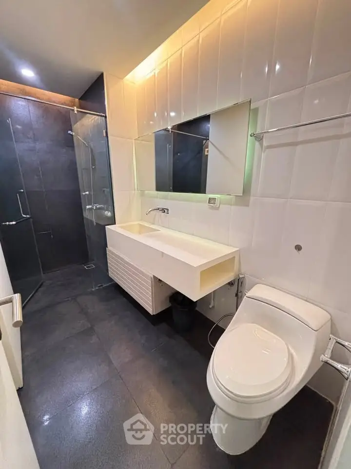 Modern bathroom with sleek design, featuring a glass shower, white vanity, and contemporary fixtures.