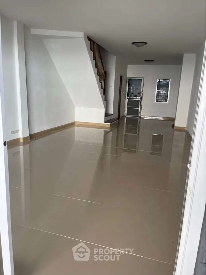 Spacious empty room with glossy tiled floors and staircase, perfect for customization.