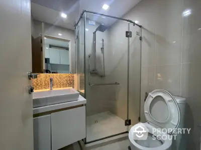 Modern bathroom with glass shower and sleek vanity in contemporary apartment.