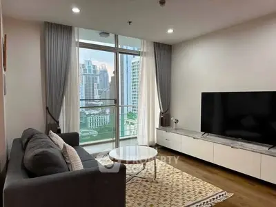 Modern living room with large TV and city view from balcony, featuring sleek furniture and elegant decor.
