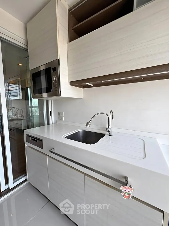 Modern kitchen with sleek cabinetry and built-in microwave, featuring a stylish sink and ample counter space.