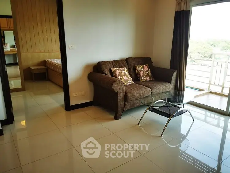 Cozy living room with brown sofa and glass coffee table, adjacent to bedroom and balcony view.