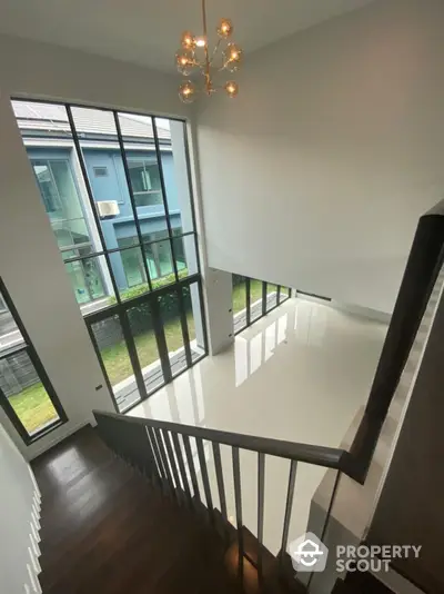 Bright and airy stairwell with large windows, modern chandelier, and sleek railing, leading to a spacious upper level in a contemporary home.