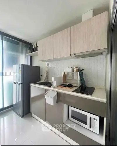 Modern kitchen with sleek cabinetry, built-in microwave, and compact fridge in a stylish apartment.