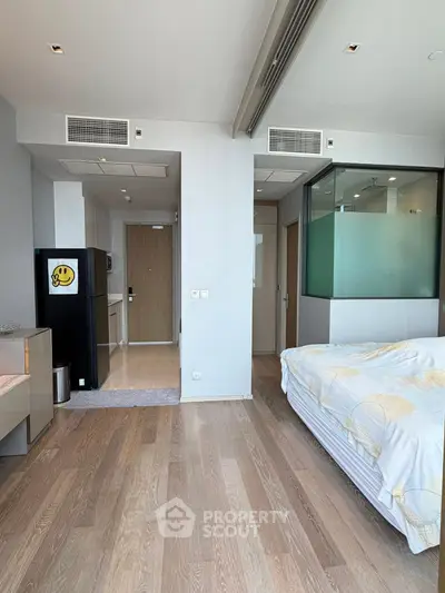 Modern studio apartment with wooden flooring, compact kitchen, and cozy sleeping area.