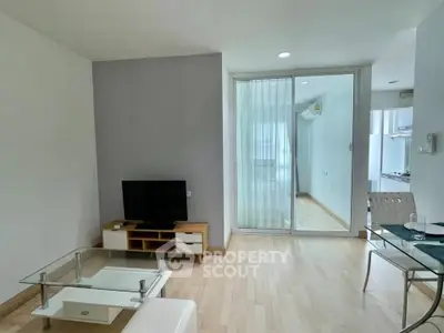Modern living room with glass coffee table and TV, featuring light wood flooring and sliding glass doors.