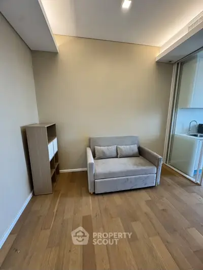 Modern living room with wooden flooring and cozy sofa, adjacent to a compact kitchen area.