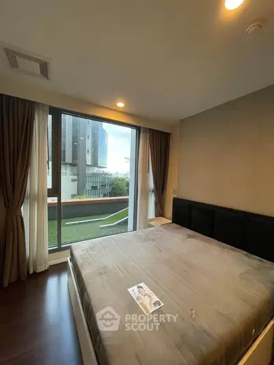 Spacious bedroom with large window and modern decor, offering a serene view of the cityscape.