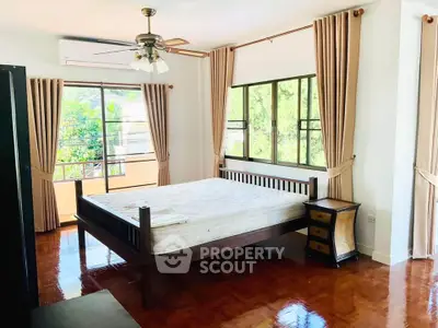 Spacious bedroom with large windows and wooden flooring, featuring a ceiling fan and elegant curtains.