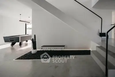 Modern minimalist interior with sleek staircase and pool table in open living space.