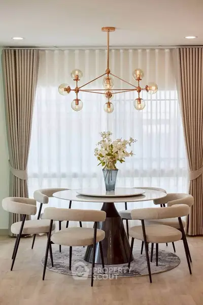 Elegant dining area with modern chandelier and stylish round table set against large windows with curtains.