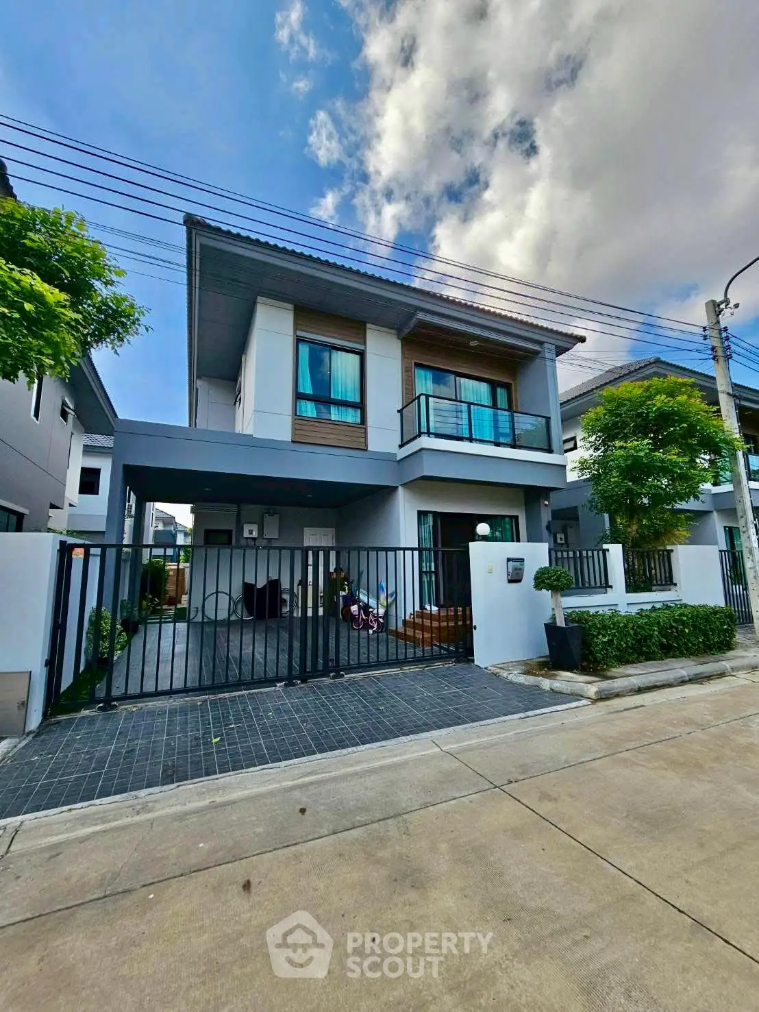 Modern two-story house with balcony and gated driveway in suburban neighborhood.