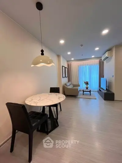Modern living room with elegant dining area and cozy seating, featuring stylish lighting and large window.