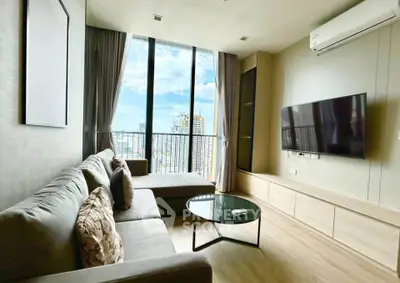 Modern living room with large windows and city view, featuring a comfortable sofa and wall-mounted TV.