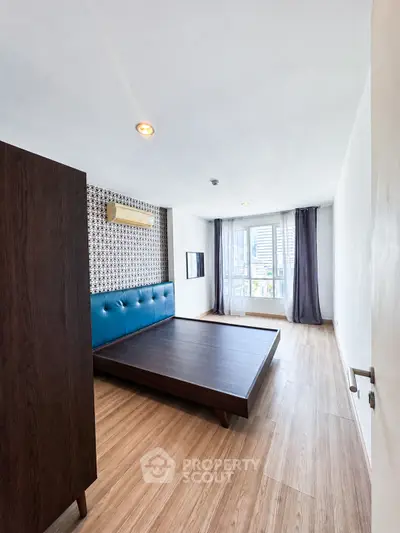Spacious modern bedroom with wooden flooring and large window for natural light.