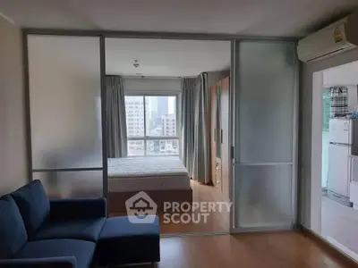 Modern apartment with sliding glass doors separating bedroom and living area, featuring city view.
