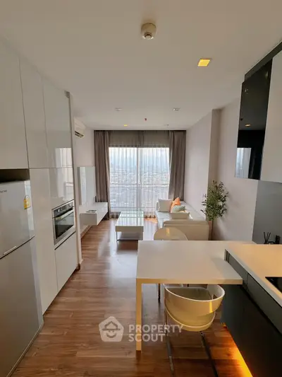 Modern living room with open kitchen and city view, featuring sleek furniture and natural light.