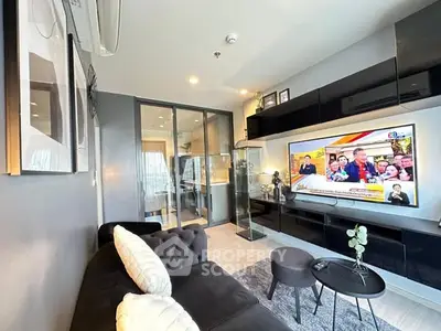 Modern living room with sleek black furniture and large TV, perfect for entertainment.
