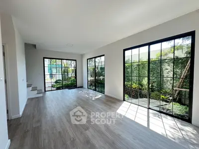 Spacious living room with large windows and garden view, featuring modern flooring and abundant natural light.