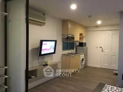 Modern apartment interior with compact kitchen and living area, featuring washing machine and wall-mounted TV.