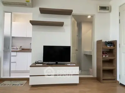 Modern living room with TV, open kitchen, and stylish shelving in a cozy apartment.