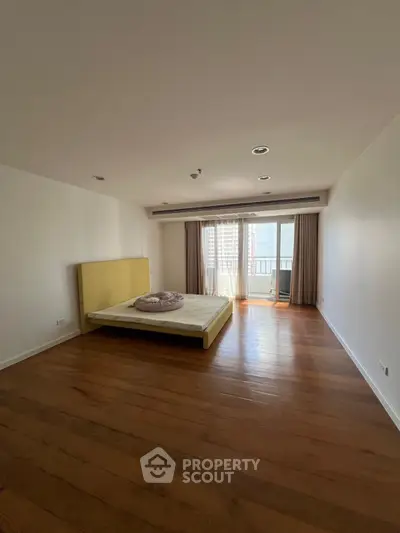 Spacious bedroom with wooden flooring and large window offering city view