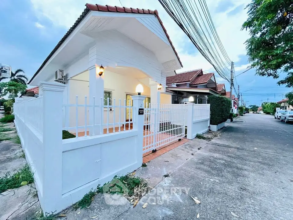 Charming white house with tiled roof and gated entrance in a peaceful suburban neighborhood.