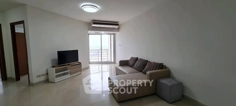 Spacious living room with modern sofa and TV, featuring a large window with city view.