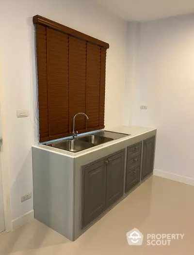 Compact kitchen space with modern gray cabinetry and stainless steel sink, complemented by warm brown window blinds in a well-lit room.