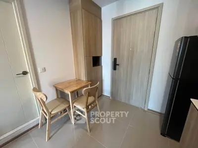 Cozy dining nook in modern apartment with wooden table and chairs, adjacent to sleek refrigerator.