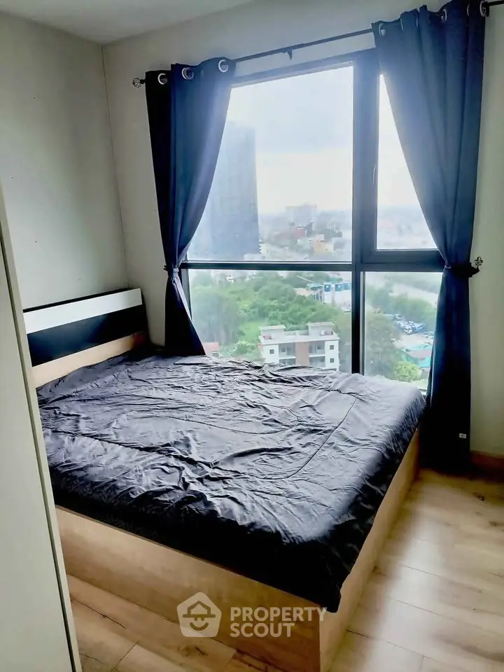 Cozy bedroom with large window offering stunning city views, featuring a comfortable bed and elegant curtains.