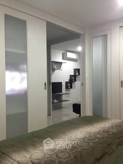 Modern bedroom with sliding doors opening to a stylish living area, featuring sleek furniture and a mounted TV.