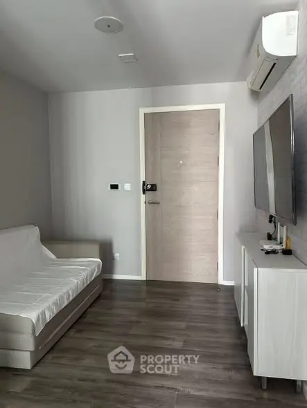 Modern living room with sleek furniture and wall-mounted TV, featuring minimalist design and air conditioning.