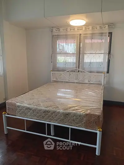 Cozy bedroom with a neatly made bed and natural light from large windows.