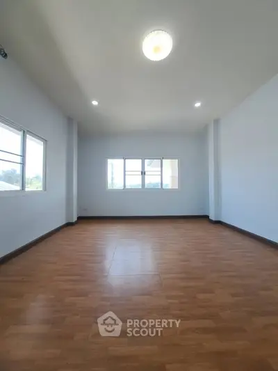 Spacious empty room with wooden flooring and large windows offering natural light.