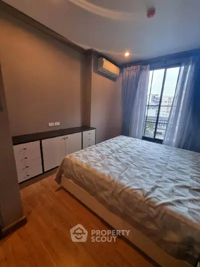 Cozy bedroom with modern decor and large window offering city views, featuring a comfortable bed and ample storage.