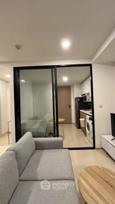 Modern living room with sliding glass doors and compact kitchen featuring a washing machine.