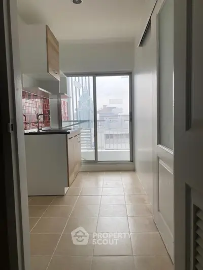 Modern kitchen with open layout and balcony view, featuring sleek cabinetry and tiled flooring.